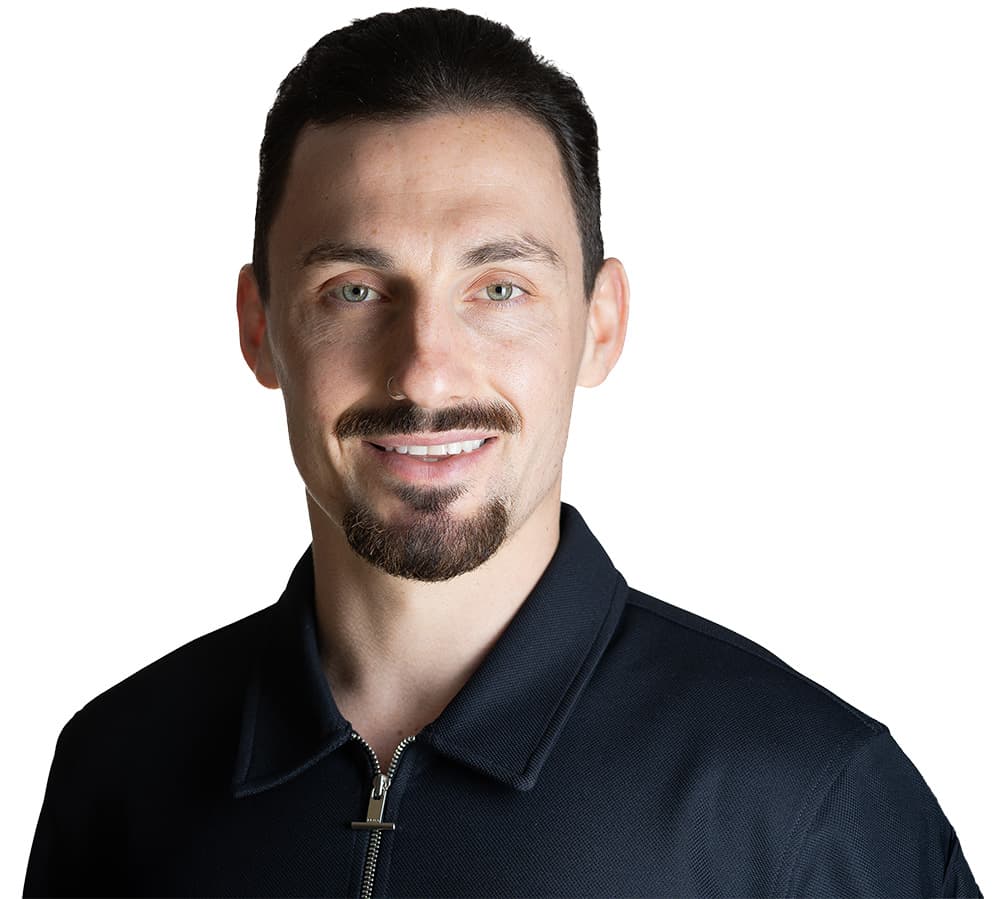 Dr Elliot Ward, chiropractor at Restore & Move, smiling in a black polo shirt